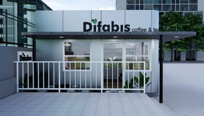 The interior of Cafe Difabis features a modern and inclusive design, incorporating wood elements and warm lighting. The ergonomic barista area is designed for accessibility, showcasing a professional coffee machine, open storage shelves, and a well-organized food display.