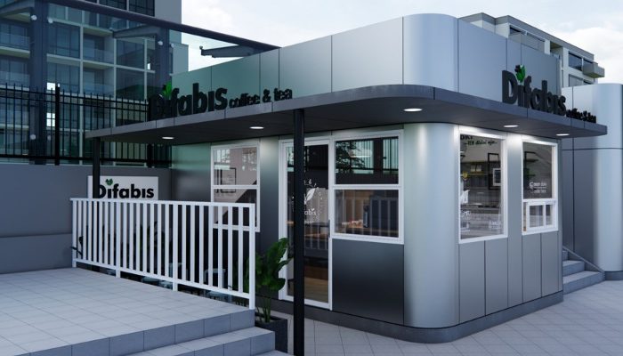 The interior of Cafe Difabis features a modern and inclusive design, incorporating wood elements and warm lighting. The ergonomic barista area is designed for accessibility, showcasing a professional coffee machine, open storage shelves, and a well-organized food display.