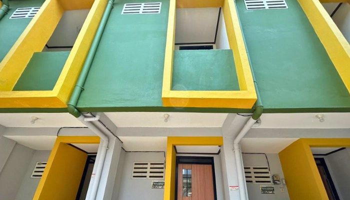 A sustainable urban housing project featuring compact modern residences, a pedestrian-friendly environment, and a landscaped public space with a pond and greenery. The area integrates eco-friendly elements such as green facades, vertical gardens, and natural ventilation.