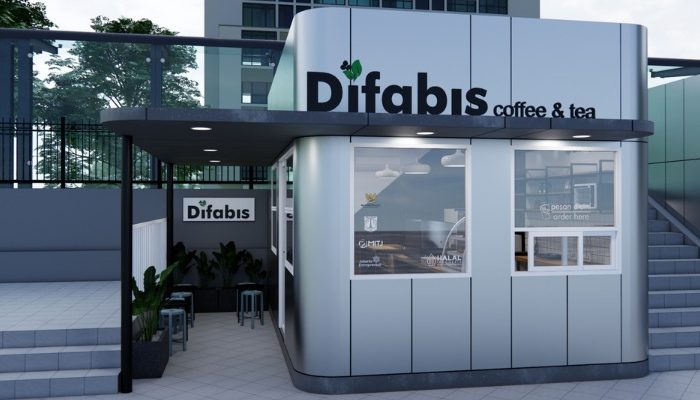 The interior of Cafe Difabis features a modern and inclusive design, incorporating wood elements and warm lighting. The ergonomic barista area is designed for accessibility, showcasing a professional coffee machine, open storage shelves, and a well-organized food display.