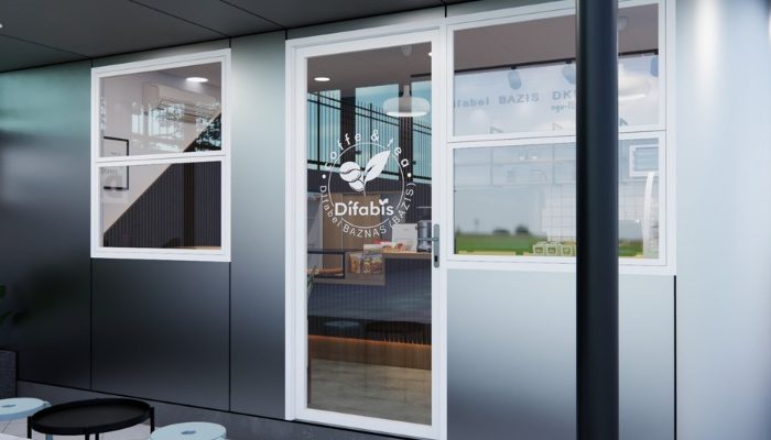 The interior of Cafe Difabis features a modern and inclusive design, incorporating wood elements and warm lighting. The ergonomic barista area is designed for accessibility, showcasing a professional coffee machine, open storage shelves, and a well-organized food display.
