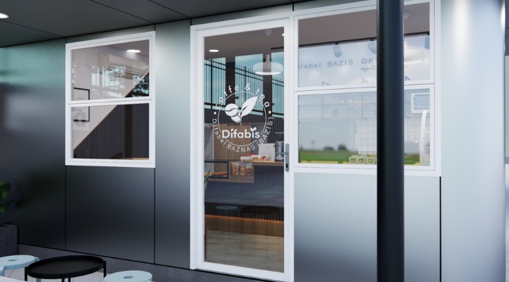 The interior of Cafe Difabis features a modern and inclusive design, incorporating wood elements and warm lighting. The ergonomic barista area is designed for accessibility, showcasing a professional coffee machine, open storage shelves, and a well-organized food display.