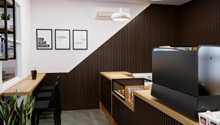 The interior of Cafe Difabis features a modern and inclusive design, incorporating wood elements and warm lighting. The ergonomic barista area is designed for accessibility, showcasing a professional coffee machine, open storage shelves, and a well-organized food display.