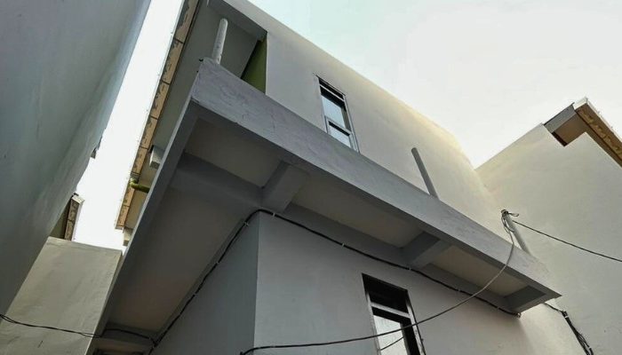 A sustainable urban housing project featuring compact modern residences, a pedestrian-friendly environment, and a landscaped public space with a pond and greenery. The area integrates eco-friendly elements such as green facades, vertical gardens, and natural ventilation.