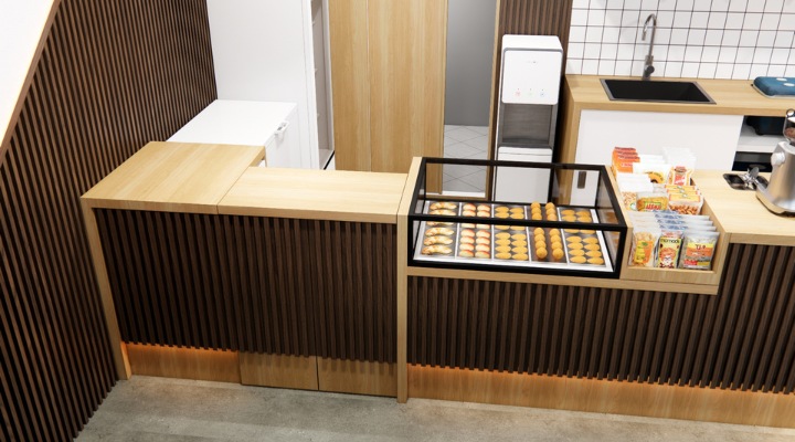 The interior of Cafe Difabis features a modern and inclusive design, incorporating wood elements and warm lighting. The ergonomic barista area is designed for accessibility, showcasing a professional coffee machine, open storage shelves, and a well-organized food display.