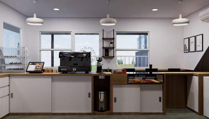 The interior of Cafe Difabis features a modern and inclusive design, incorporating wood elements and warm lighting. The ergonomic barista area is designed for accessibility, showcasing a professional coffee machine, open storage shelves, and a well-organized food display.
