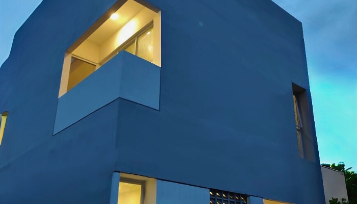 The main façade and interior of WU House in North Jakarta, featuring a tropical modern design with exposed concrete materials, natural wood, and large glass openings that optimize natural lighting and air circulation.