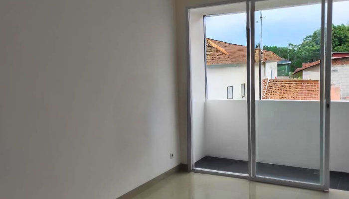The main façade and interior of WU House in North Jakarta, featuring a tropical modern design with exposed concrete materials, natural wood, and large glass openings that optimize natural lighting and air circulation.