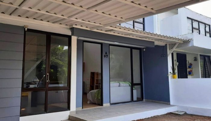 Front view of a modern two-story tropical house in Bintaro with large windows, a soft blue façade, and a functional carport integrated into the minimalist design.