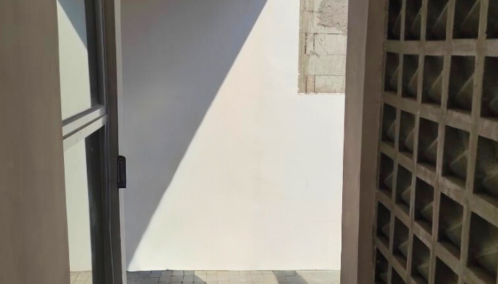 The main façade and interior of WU House in North Jakarta, featuring a tropical modern design with exposed concrete materials, natural wood, and large glass openings that optimize natural lighting and air circulation.
