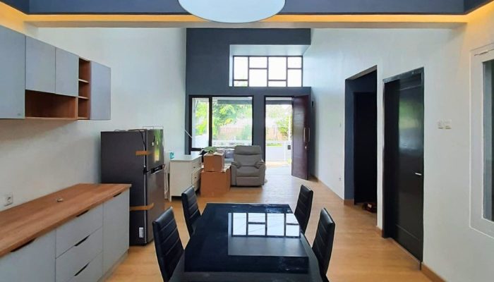Front view of a modern two-story tropical house in Bintaro with large windows, a soft blue façade, and a functional carport integrated into the minimalist design.