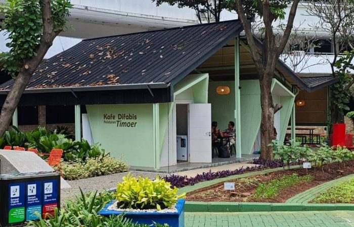 Tampak bangunan Café Difabis Coffee & Bakery karya YPA Architecture Studio di kawasan Kantor Walikota Jakarta Timur dengan atap pelana asimetris, façade hijau pastel, dan area terbuka yang ramah bagi semua pengguna.