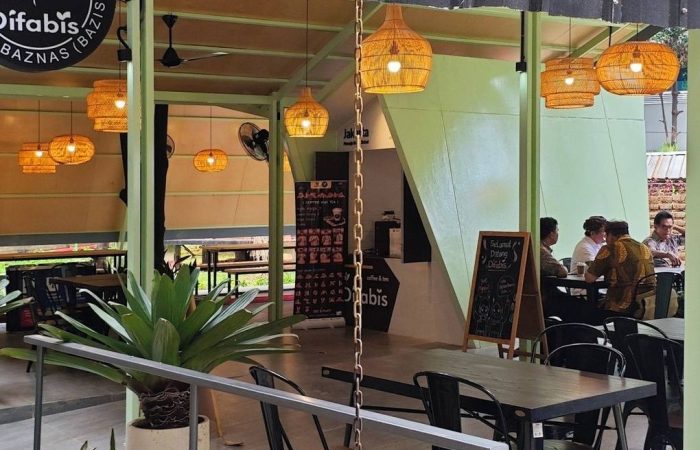 Tampak bangunan Café Difabis Coffee & Bakery karya YPA Architecture Studio di kawasan Kantor Walikota Jakarta Timur dengan atap pelana asimetris, façade hijau pastel, dan area terbuka yang ramah bagi semua pengguna.