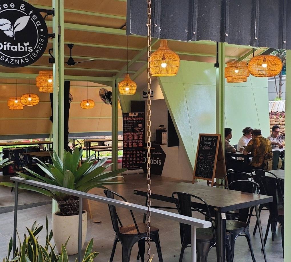 Tampak bangunan Café Difabis Coffee & Bakery karya YPA Architecture Studio di kawasan Kantor Walikota Jakarta Timur dengan atap pelana asimetris, façade hijau pastel, dan area terbuka yang ramah bagi semua pengguna.