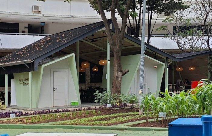 Tampak bangunan Café Difabis Coffee & Bakery karya YPA Architecture Studio di kawasan Kantor Walikota Jakarta Timur dengan atap pelana asimetris, façade hijau pastel, dan area terbuka yang ramah bagi semua pengguna.