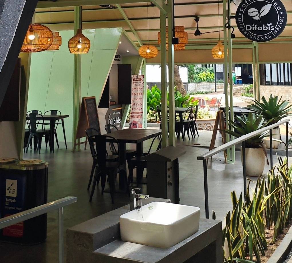 Tampak bangunan Café Difabis Coffee & Bakery karya YPA Architecture Studio di kawasan Kantor Walikota Jakarta Timur dengan atap pelana asimetris, façade hijau pastel, dan area terbuka yang ramah bagi semua pengguna.