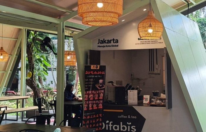 Tampak bangunan Café Difabis Coffee & Bakery karya YPA Architecture Studio di kawasan Kantor Walikota Jakarta Timur dengan atap pelana asimetris, façade hijau pastel, dan area terbuka yang ramah bagi semua pengguna.