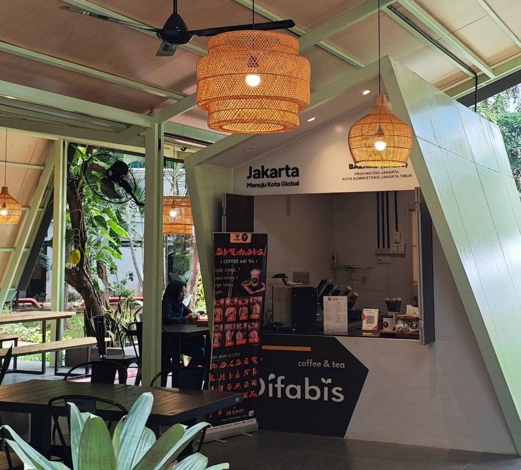 Tampak bangunan Café Difabis Coffee & Bakery karya YPA Architecture Studio di kawasan Kantor Walikota Jakarta Timur dengan atap pelana asimetris, façade hijau pastel, dan area terbuka yang ramah bagi semua pengguna.