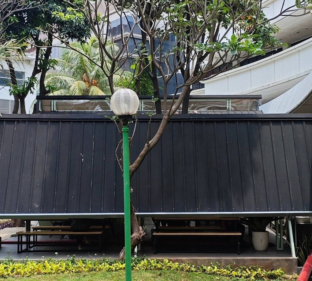 Tampak bangunan Café Difabis Coffee & Bakery karya YPA Architecture Studio di kawasan Kantor Walikota Jakarta Timur dengan atap pelana asimetris, façade hijau pastel, dan area terbuka yang ramah bagi semua pengguna.