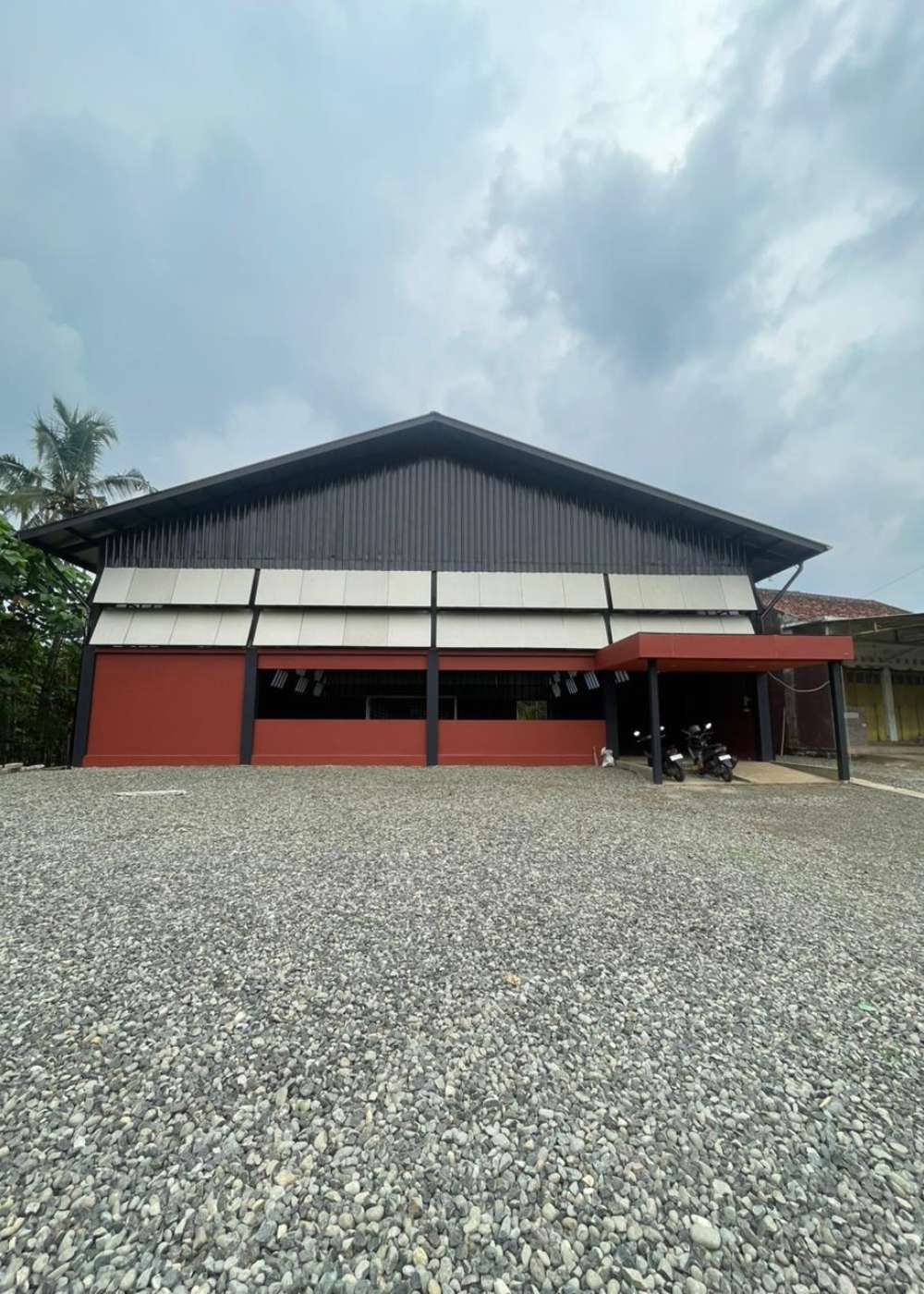 Eksterior bangunan Panunggalan Dream Futsal di Purbalingga karya YPA Architecture Studio dengan fasad merah bata dan hitam, atap pelana metal, serta area parkir luas.